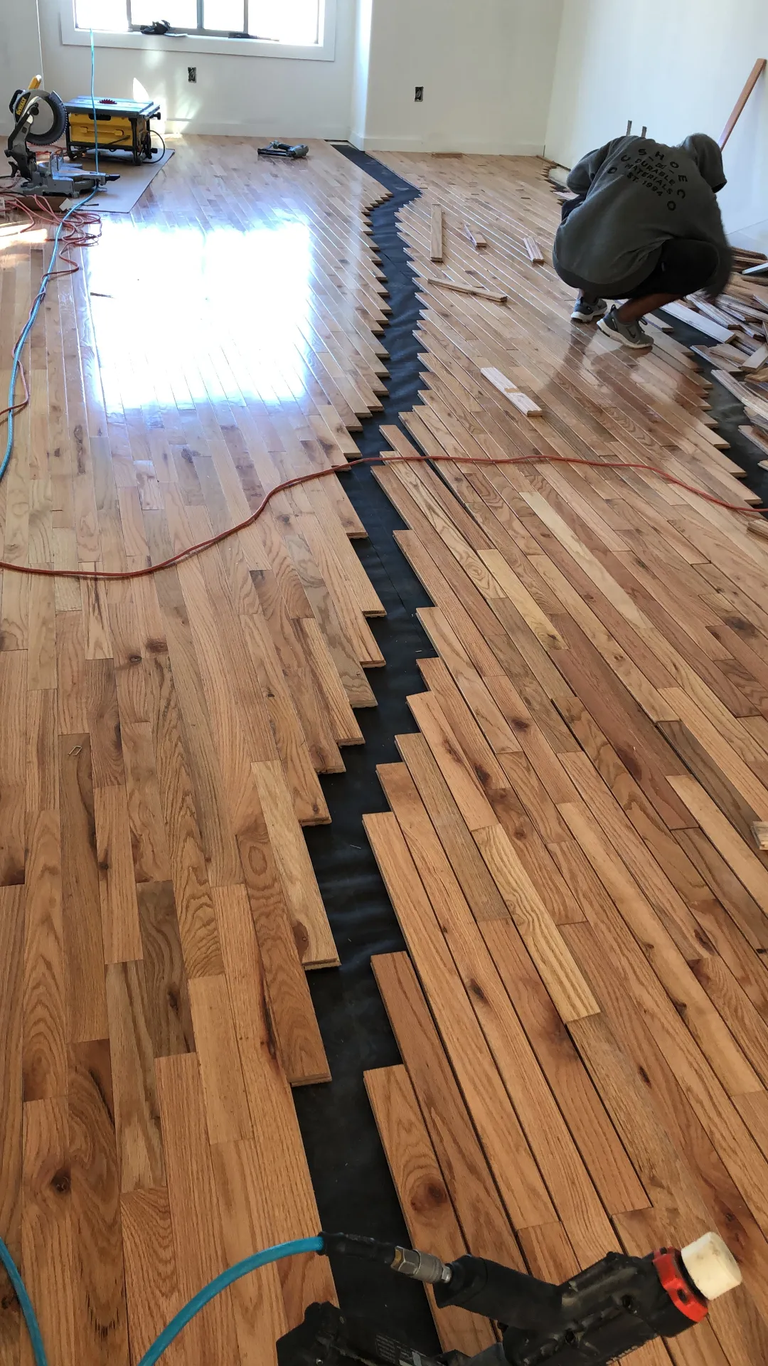 Red oak strip hardwood floor installation in progress over black underlayment